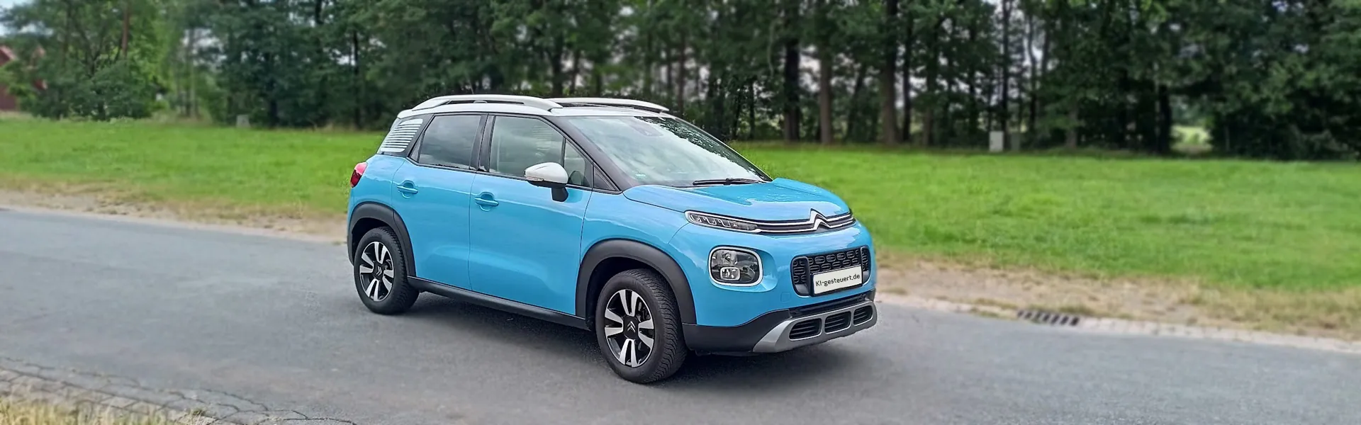 Bild 3: Ki-gesteuerter hellblauer Citroen C3 Aircross mit weißem Dach fährt auf einer Strasse vor Bäumen